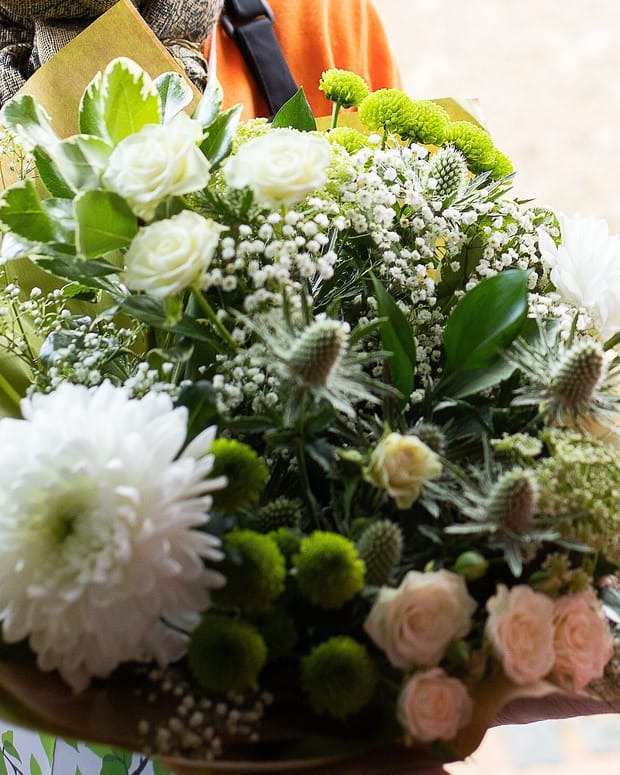 A wrapped white and green hand-tied bouquet passing from one pair of hands to another.