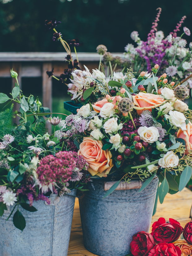 Two galvanised buckets of garden roses, sedum and astrantia standing on the workshop bench.