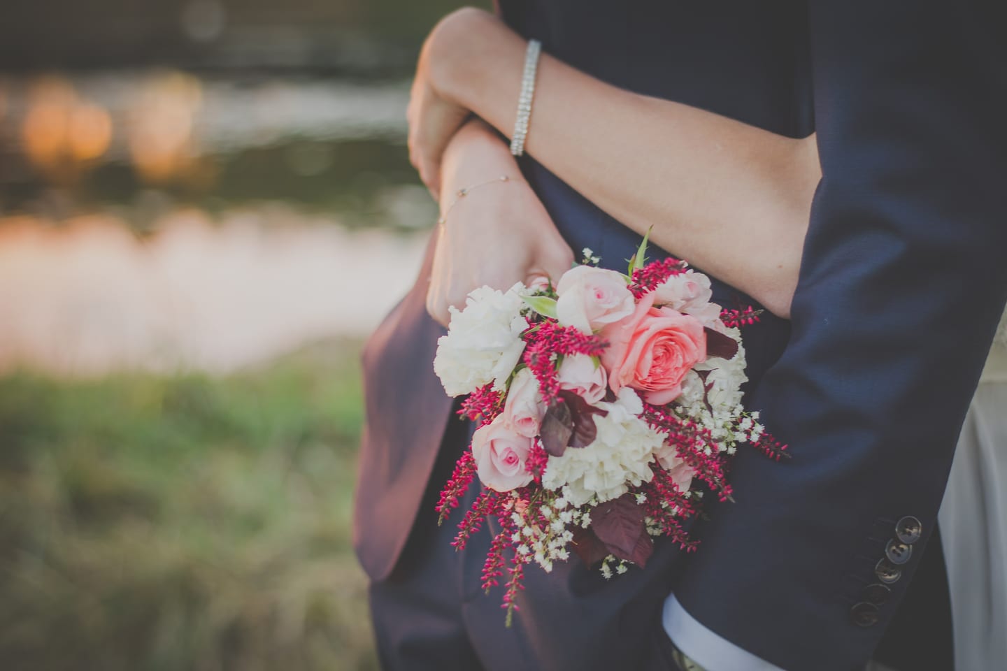 A person in a dark suit holding a blush bouquet of roses and gypsophila, hands and sleeve only.