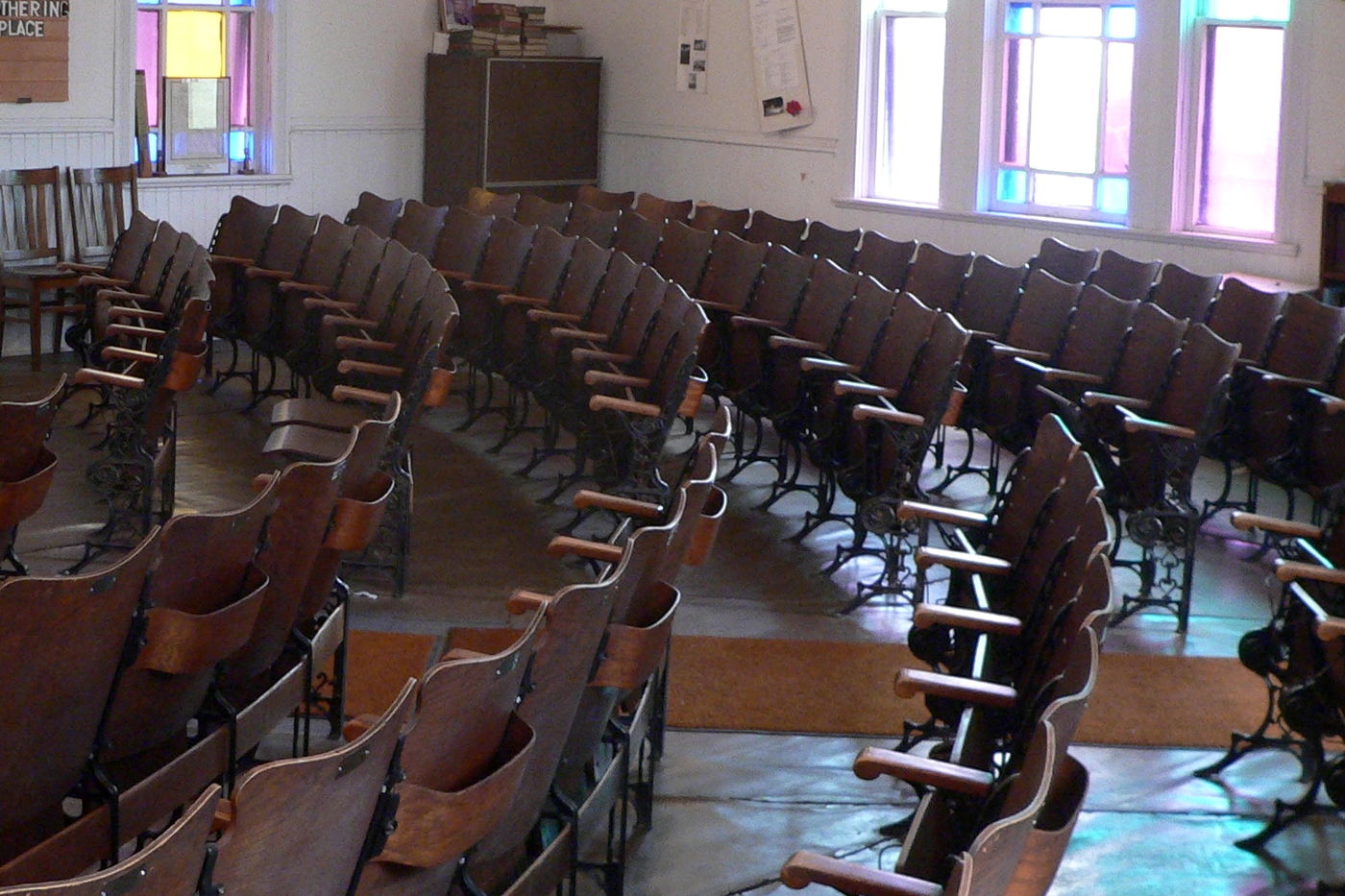 Curved rows of dark wooden seats on cast-iron frames under stained-glass windows.