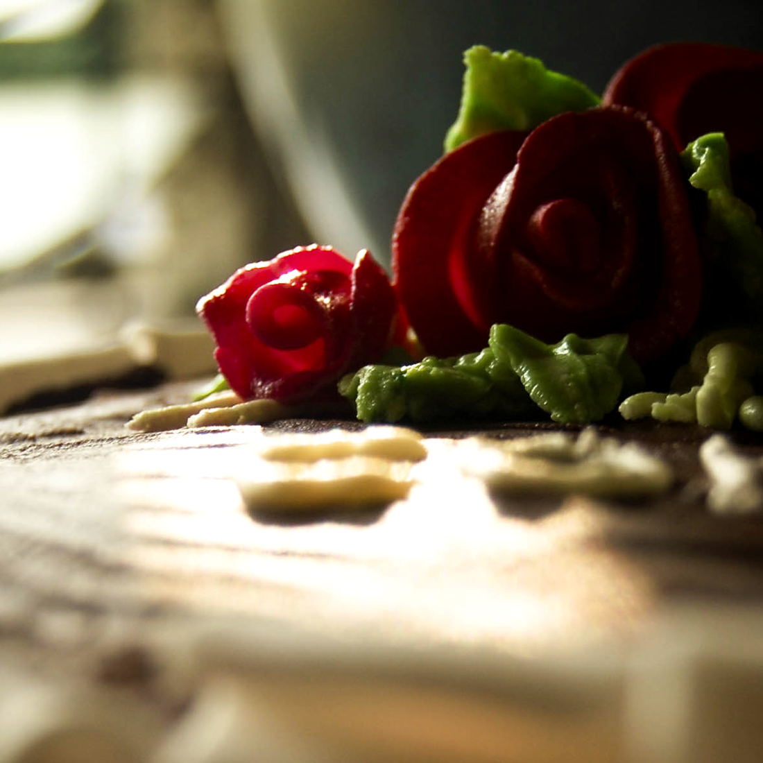 Red sugar-paste roses with green leaves laid out on a wooden board, photographed close and backlit.