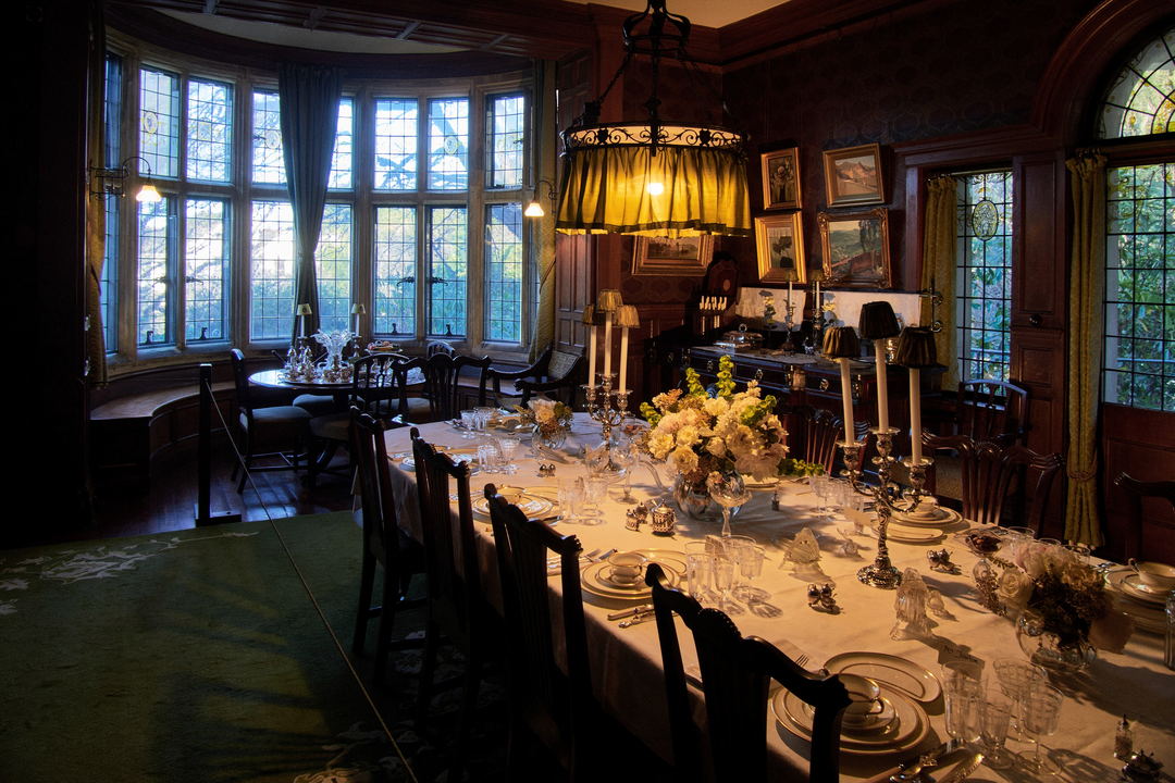 A panelled dining hall in a historic house, with a long table set under tall windows.