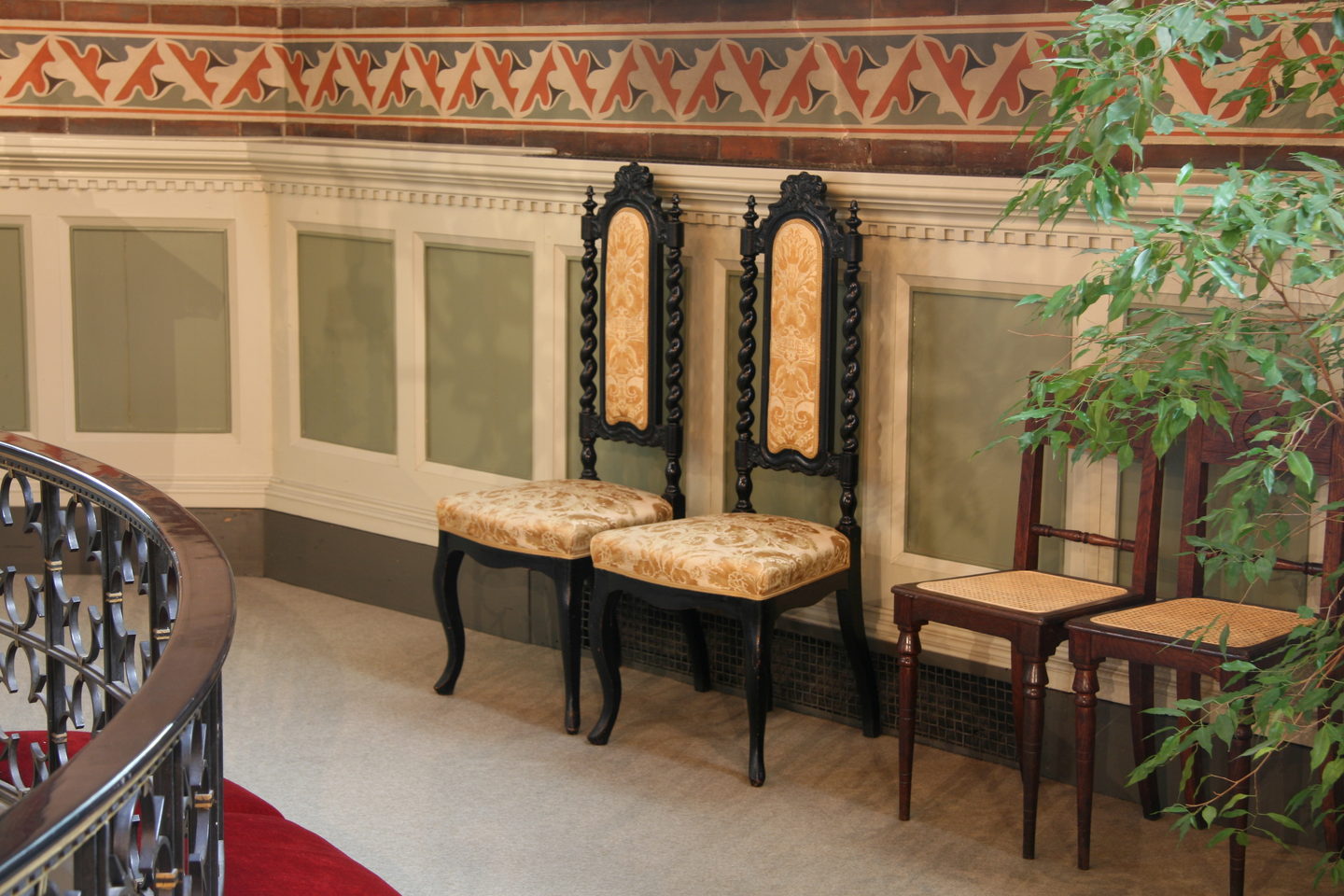 Two high-backed bridal chairs upholstered in gold damask, set against the painted wall of a church.