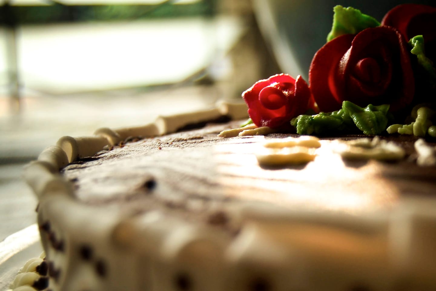 A close view of the edge of a cake decorated with red sugar-paste roses and green leaves.