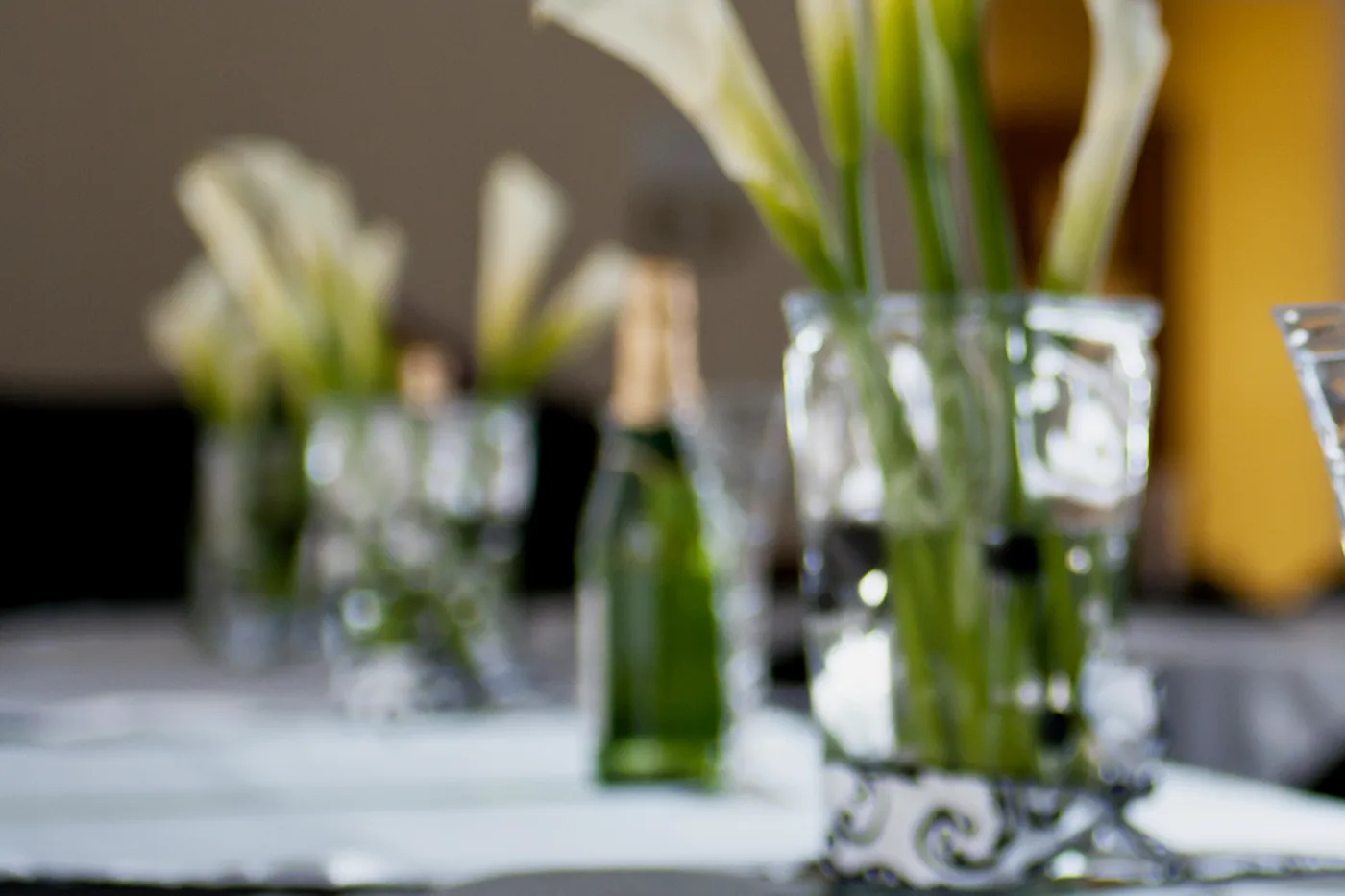 Calla lilies, glassware and a chilled bottle on a white linen service table.