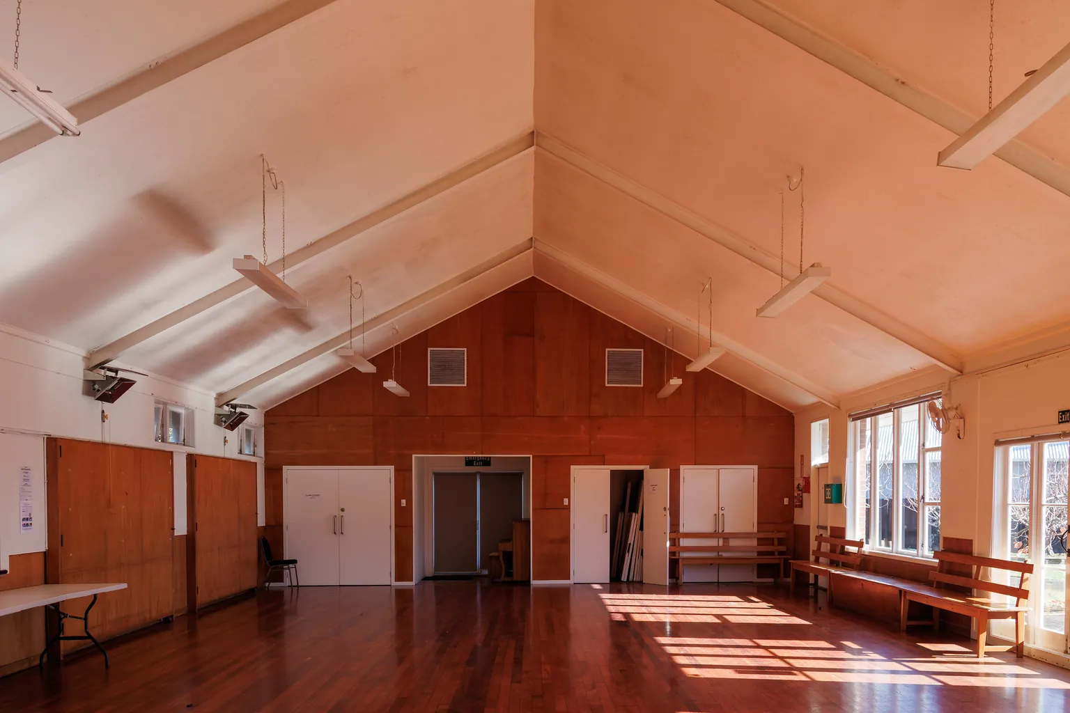 An empty timber community hall with folding tables and benches at the edges