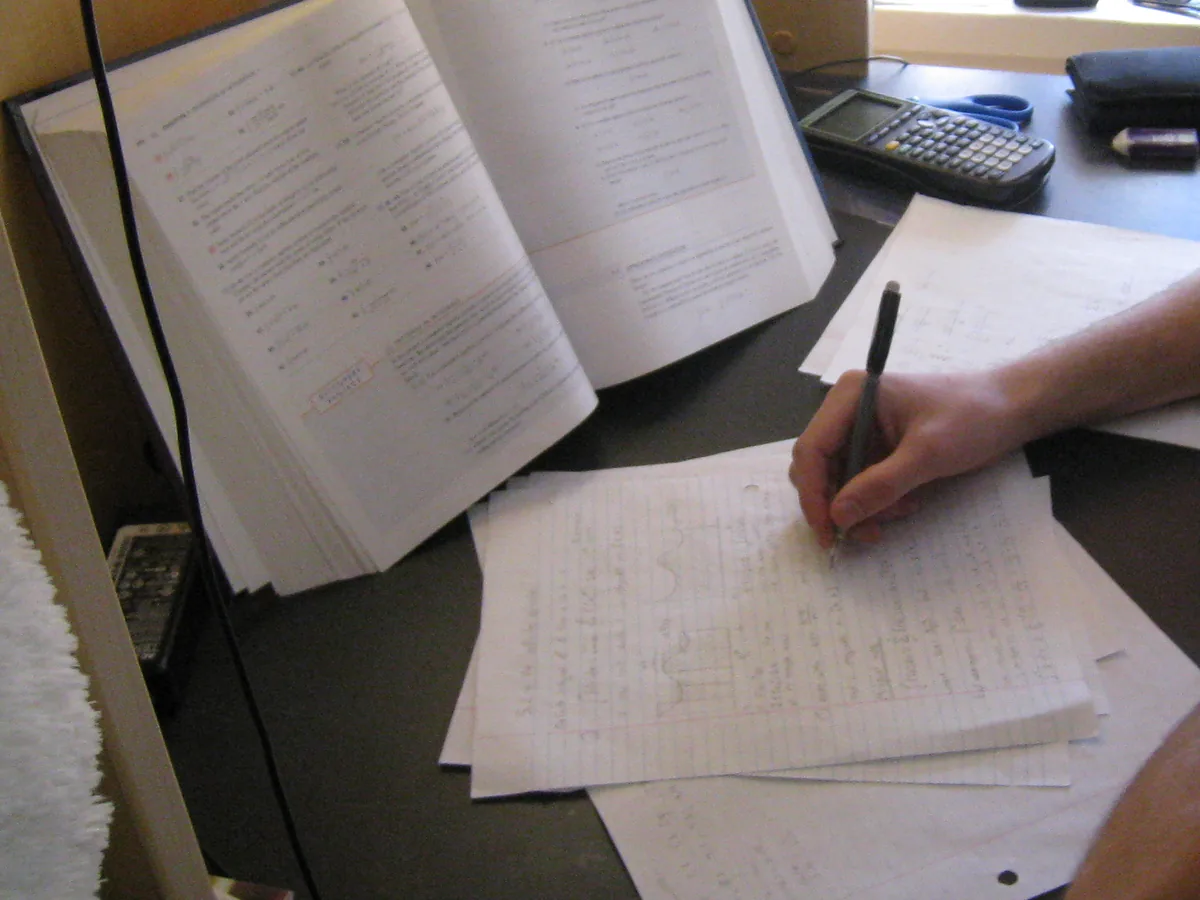 An open textbook on a stand beside worked pages and a pen